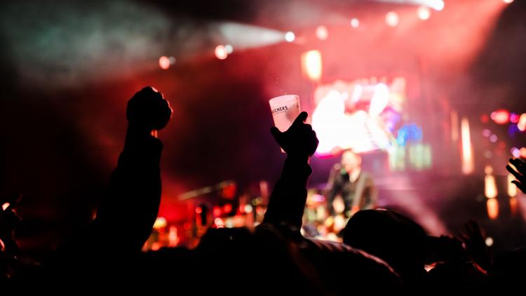 Silhouettes of crowd's raised hands holding a beer cup at Sessions gig