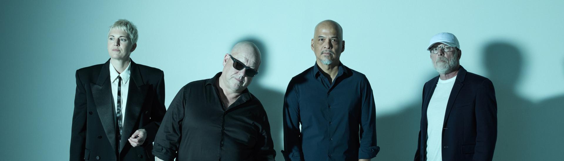 Pixies band standing against a pale duck egg blue background
