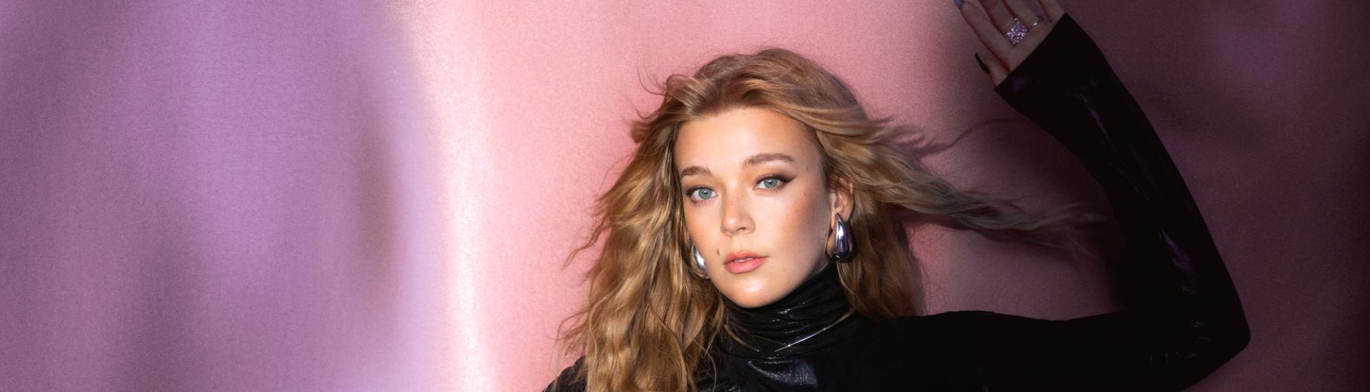 Singer Becky Hill stood against coloured drape