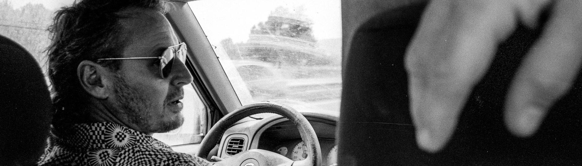Black and white photo of Ben Howard driving a car taken from the back seat